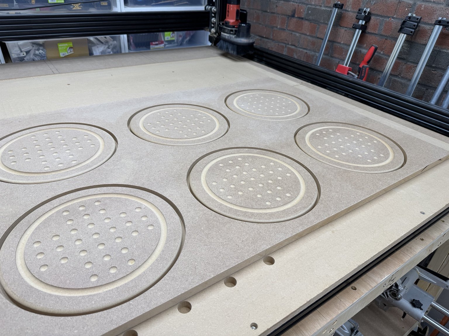 Angled workshop view of repeated routed solitaire-board components in MDF