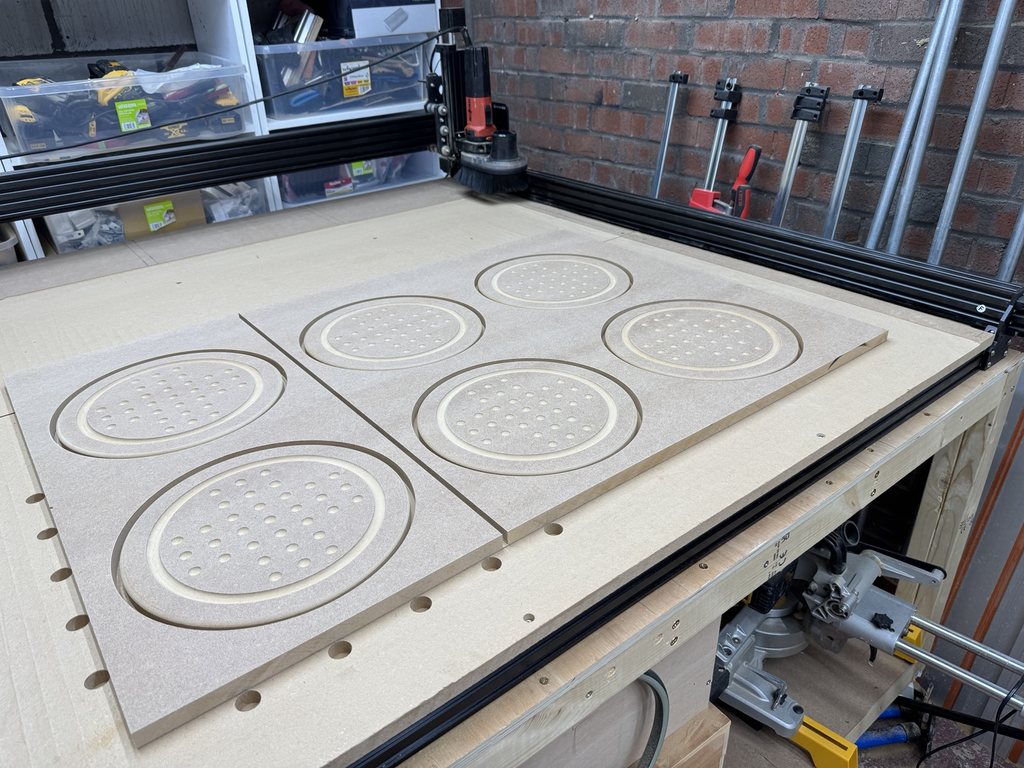 Six repeated solitaire-board components machined across sheet material before separation